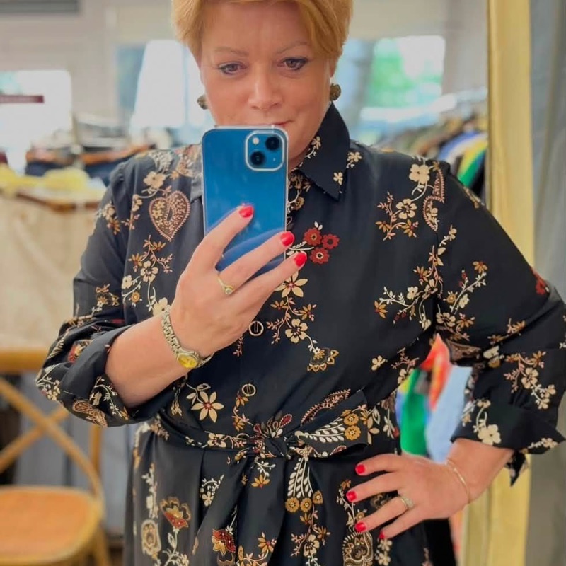 Juoda marškininio kirpimo suknelė su kreminiu ir rusvu folkloriniu gėlių raštu, surišta juosta per liemenį